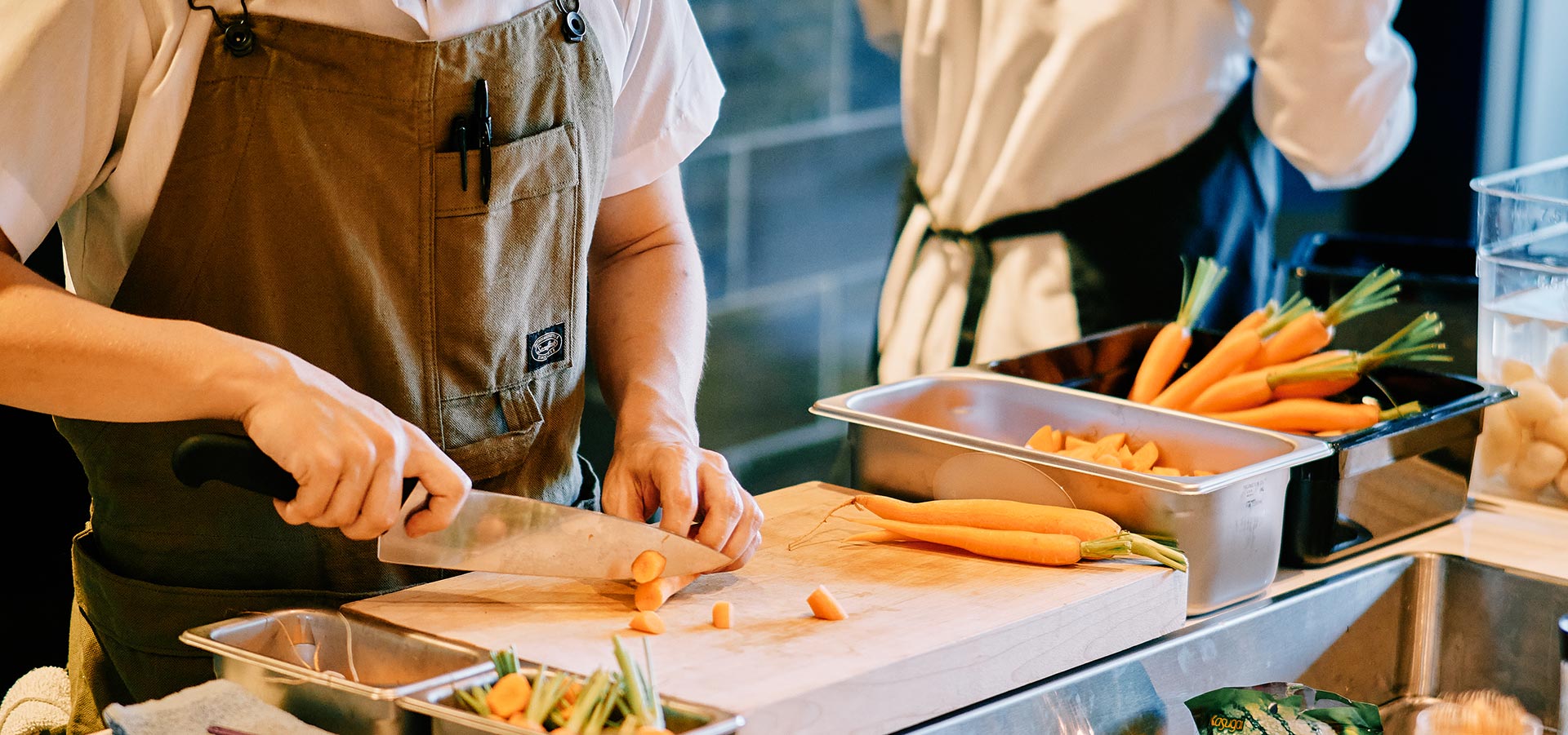 A Takibi cook chops fresh carrots at their prep station.